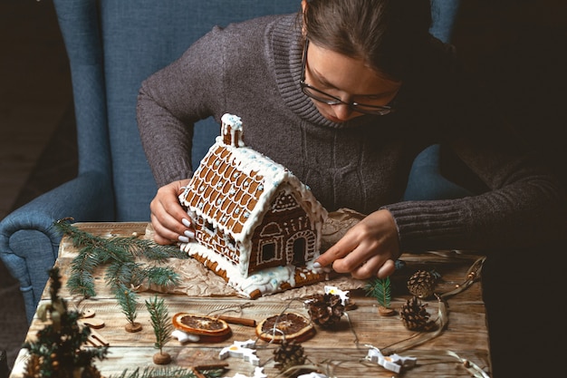 Des mains féminines décorent la maison en pain d'épice de Noël