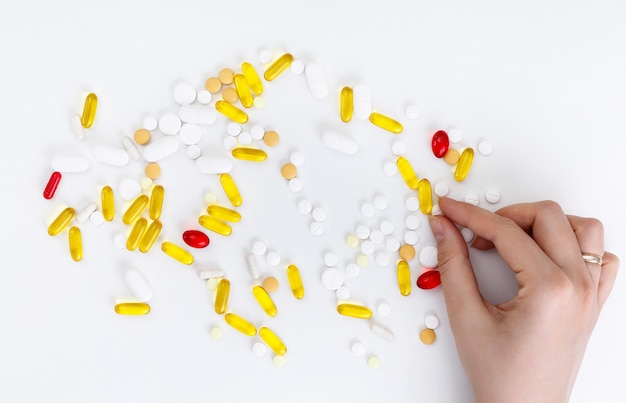 Des mains féminines détiennent des pilules multicolores sur fond blanc. Vue de dessus. Concept de santé.