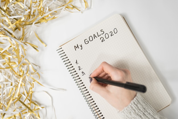 Mains féminines écrit mes objectifs 2020 dans un cahier, clinquant, concept du nouvel an