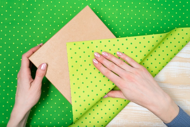 Mains féminines emballent un cadeau dans un papier à pois vert, vue de dessus