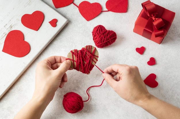 Mains féminines faisant la Saint-Valentin à partir de fil de laine sur fond blanc, coeur rouge fait maison pour la Saint-Valentin.