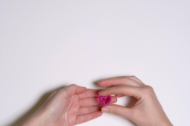 les mains féminines sur fond blanc tiennent un coeur en verre de couleur rose