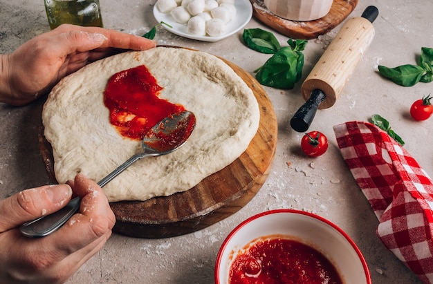 Les mains féminines font de la pizza les ingrédients pour la pizza margherita maison sur la surface de la pierre