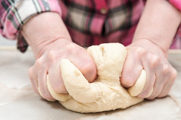 Les mains féminines avec force pétrissent la pâte sur la table, gros plan