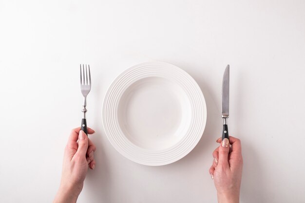 Mains féminines avec fourchette, couteau et assiette vide sur blanc