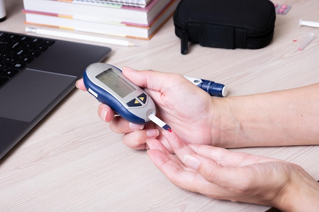 Mains féminines avec un glucomètre au bureau Le mode de vie d'une personne atteinte de diabète mesurant le niveau de glucose dans le sang