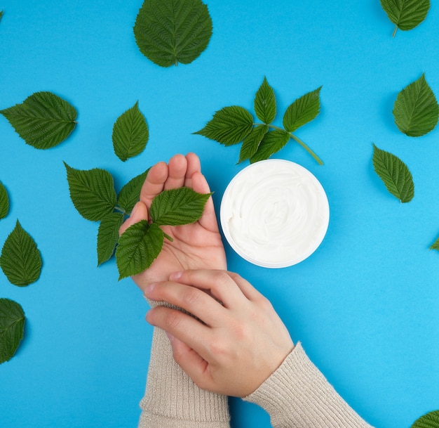 Mains féminines d'une jeune fille à la peau lisse et pot rond de crème