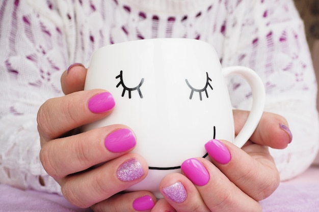 Mains féminines avec manucure lilas tenant une tasse