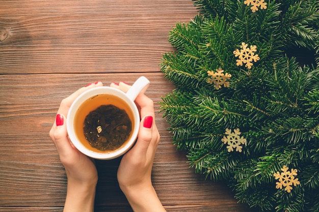 Mains féminines avec manucure rouge tenant une tasse de thé sur un fond de décorations de Noël