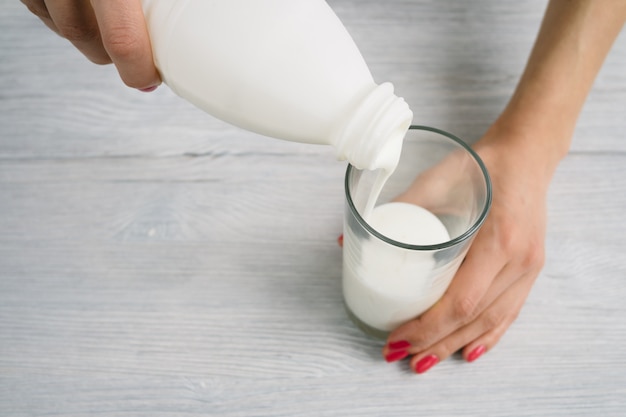 Des mains féminines avec une manucure rouge verser le yaourt dans un verre