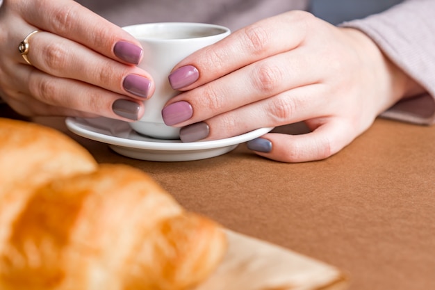 Mains féminines avec manucure tenant une tasse de café et manger un croissant. Petit déjeuner à la française