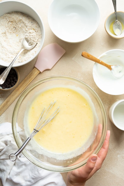 Mains féminines mélangeant les ingrédients pour la cuisson du gâteau dans un bol en verre, vue de dessus. Recette pas à pas.