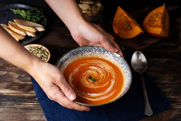 Mains féminines mettant une assiette de soupe à la crème de citrouille sur une table en bois, nourriture végétarienne saine.