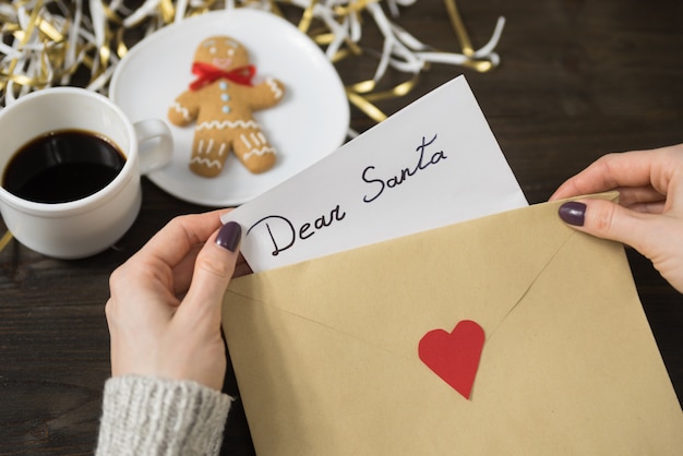 Des mains féminines mettent une lettre pour le père Noël dans une enveloppe, pain d'épice et café