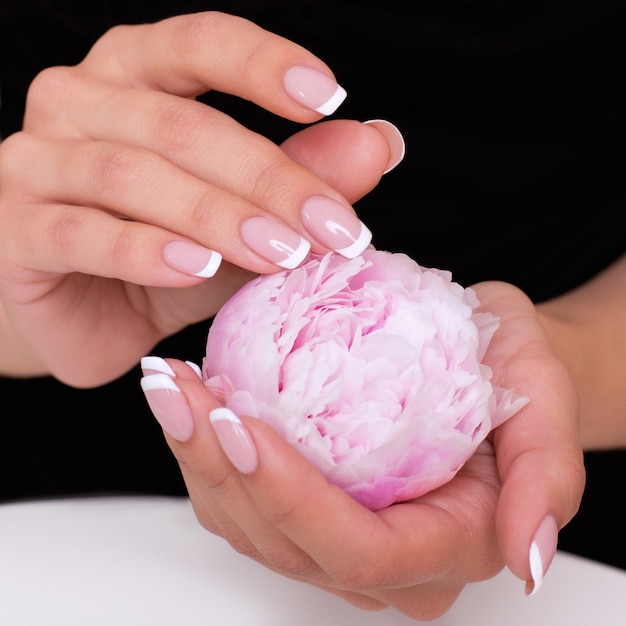 Mains féminines avec des ongles de manucure français tenant des pivoines