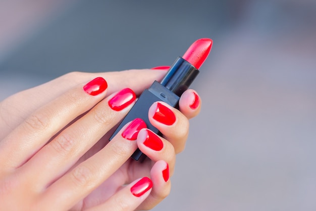 Mains féminines avec des ongles de manucure rouges tenant du rouge à lèvres