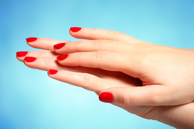 mains féminines avec des ongles peints en rouge sur fond bleu