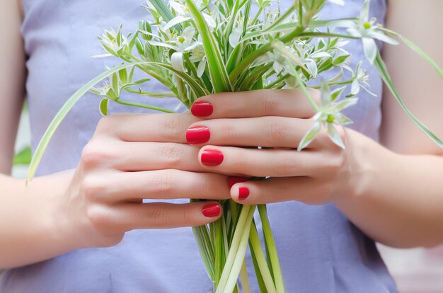 Mains féminines avec des ongles roses tenant un bouquet de fleurs