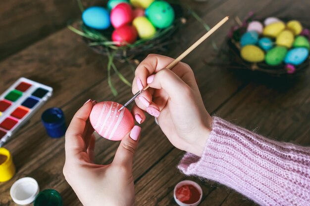 Mains féminines peignant des oeufs de Pâques sur une table en bois sombre