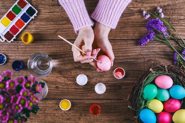 Mains féminines peignant des oeufs de Pâques sur une table en bois.