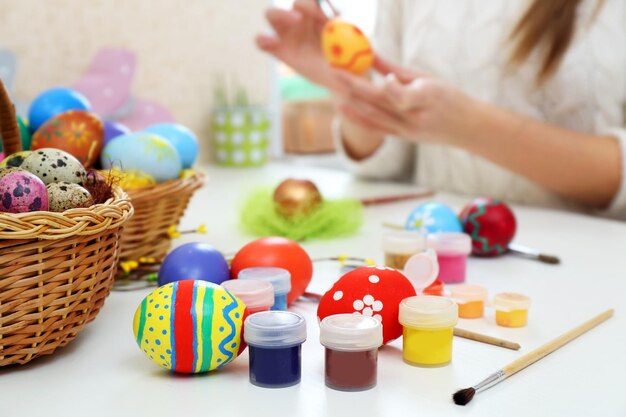 Des mains féminines peignent des œufs de Pâques à la table à l'intérieur