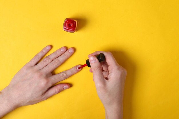 Les mains féminines peignent les ongles avec du vernis à ongles rouge sur fond jaune