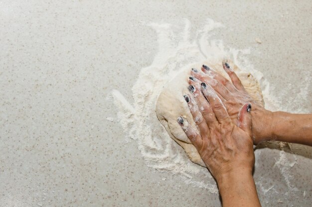 Photo des mains féminines pétrissent la pâte avec de la farine sur une table de cuisine blanche vue du haut de l'étape de préparation de la cuisson