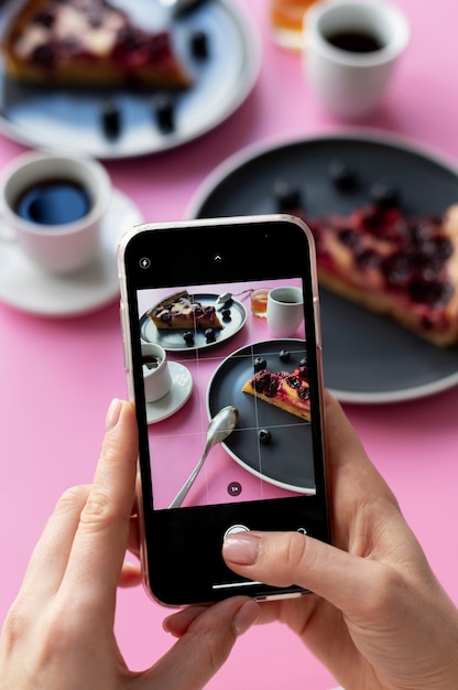 Photo mains féminines prenant la photo de deux tranches de tarte aux cerises et de deux tasses à café