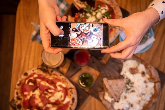 des mains féminines prennent des photos sur une table de smartphone avec une délicieuse pizza dans un restaurant. vue de dessus