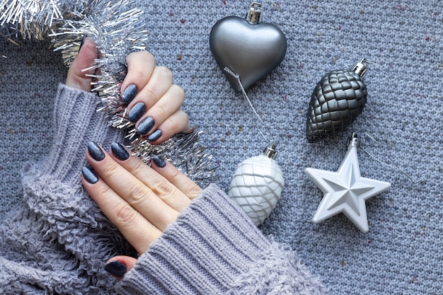 Mains féminines en pull avec des ongles scintillants bleus