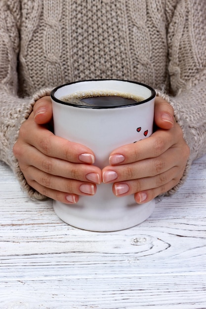 Des mains féminines avec un pull tricoté à boire du café