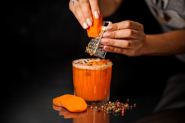 Mains féminines râpant les carottes dans le cocktail sain au poivre