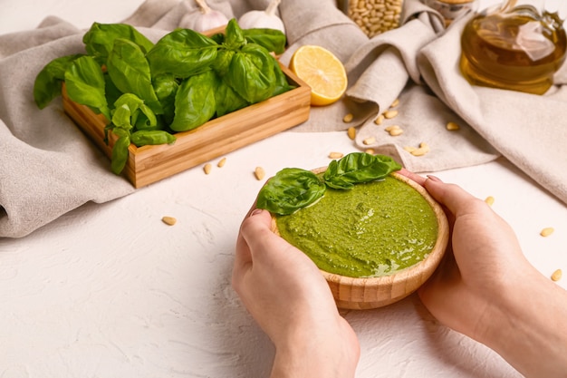 Mains féminines avec sauce pesto dans un bol sur blanc