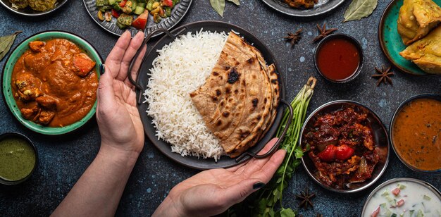 Mains féminines servant un buffet de cuisine ethnique indienne sur une table en béton rustique