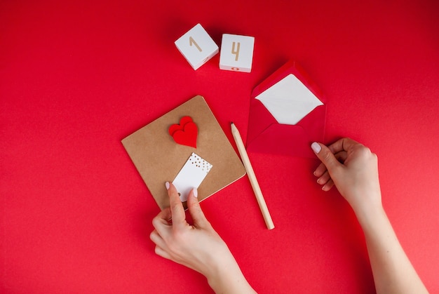 Les mains féminines signent une carte. Concept de la Saint-Valentin. Valentine, coeurs, crayon, cubes en bois avec numéro 14 de février