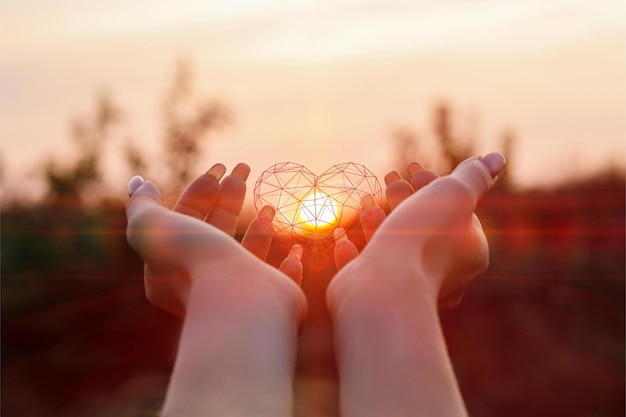 Les mains féminines soutiennent le cœur sur le fond du soleil