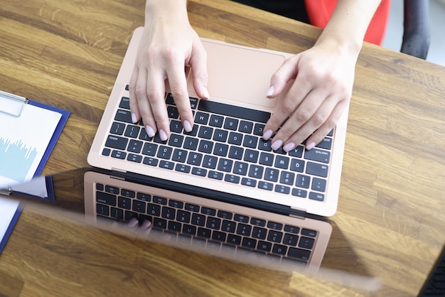 Les mains féminines tapent sur le clavier de l'ordinateur portable à table en gros plan de bureau. Travail à distance au concept de la maison.