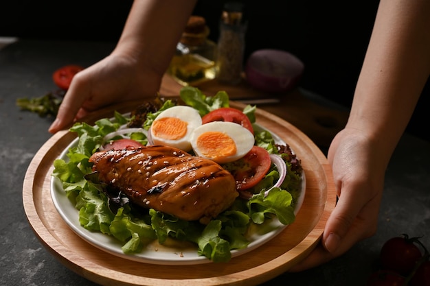 Mains féminines tenant une assiette de poitrine de poulet rôtie avec salade bio fraîche