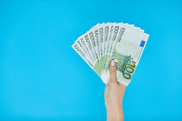 Mains féminines tenant des billets en euros sur bleu.