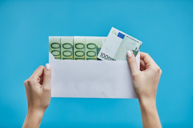 Mains féminines tenant des billets en euros dans une enveloppe