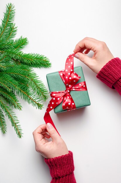 Mains féminines tenant une boîte-cadeau de Noël avec un arc rouge sur fond blanc