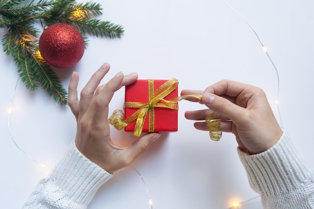 Mains féminines tenant une boîte-cadeau rouge attachée avec un ruban d'or. concept de cadeaux pour Noël et nouvel an.