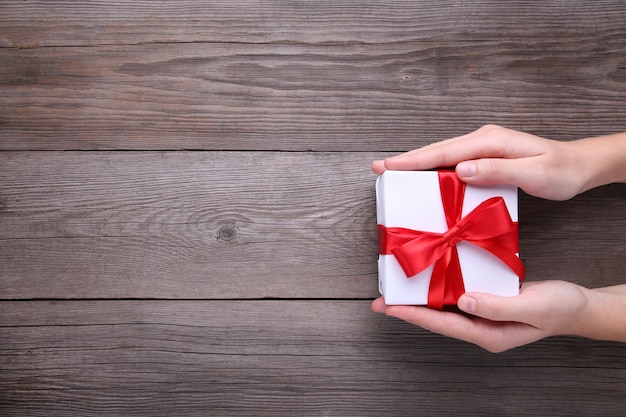 Mains féminines tenant une boîte cadeau sur une table en bois grise