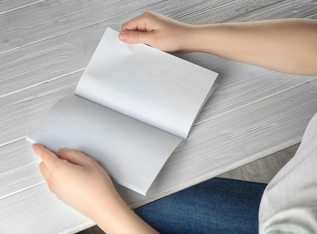 Mains féminines tenant une brochure vierge sur une table en bois blanche