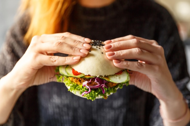 Mains féminines tenant un burger au poulet frais cuit à la vapeur avec une salade de concombre frais et un concept de restauration rapide au chou