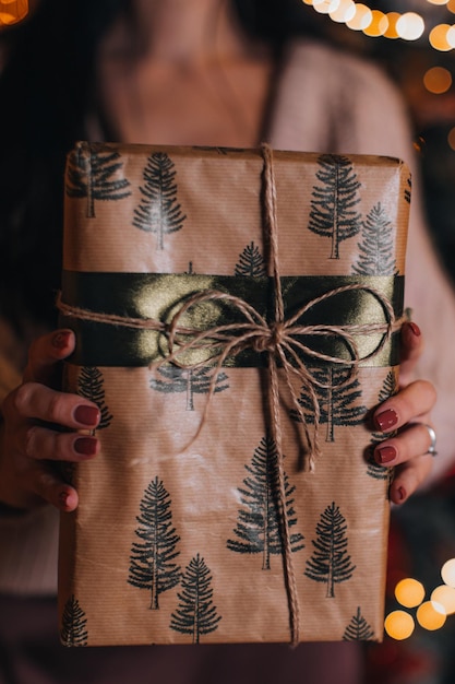 Photo des mains féminines tenant un cadeau de noël enveloppé dans du papier beige festif des vacances d'hiver festives