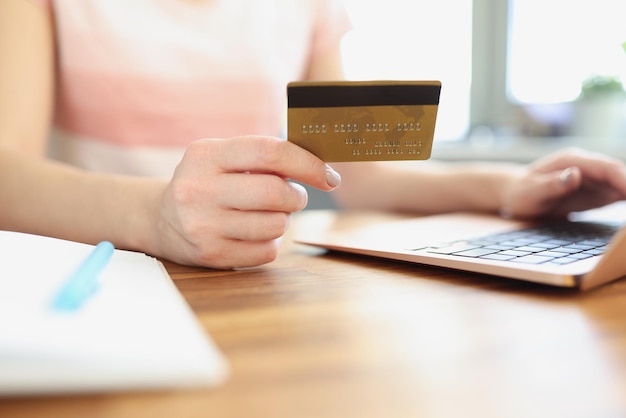 Mains féminines tenant une carte bancaire de crédit devant un ordinateur portable en gros plan