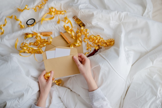 Mains féminines tenant carte-cadeau, enveloppe et boîte-cadeau sur la couverture de lit. Notion de nouvel an et de Noël. Vue horizontale supérieure