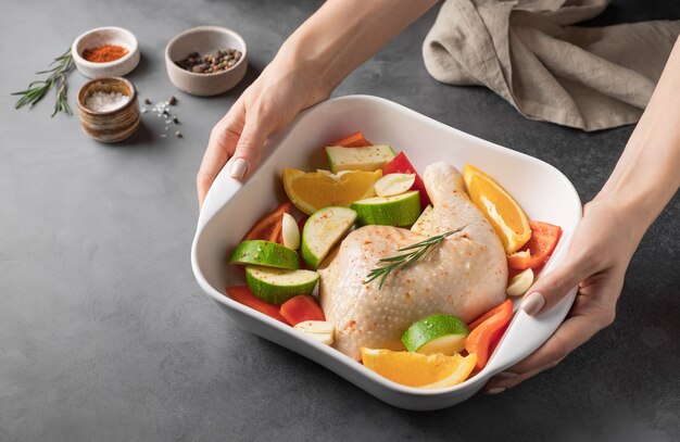 Mains féminines tenant une casserole en céramique avec de la viande de poulet crue et des légumes dîner festif