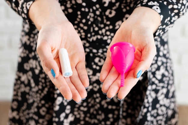 Mains féminines tenant une coupe menstruelle et un tampon médical